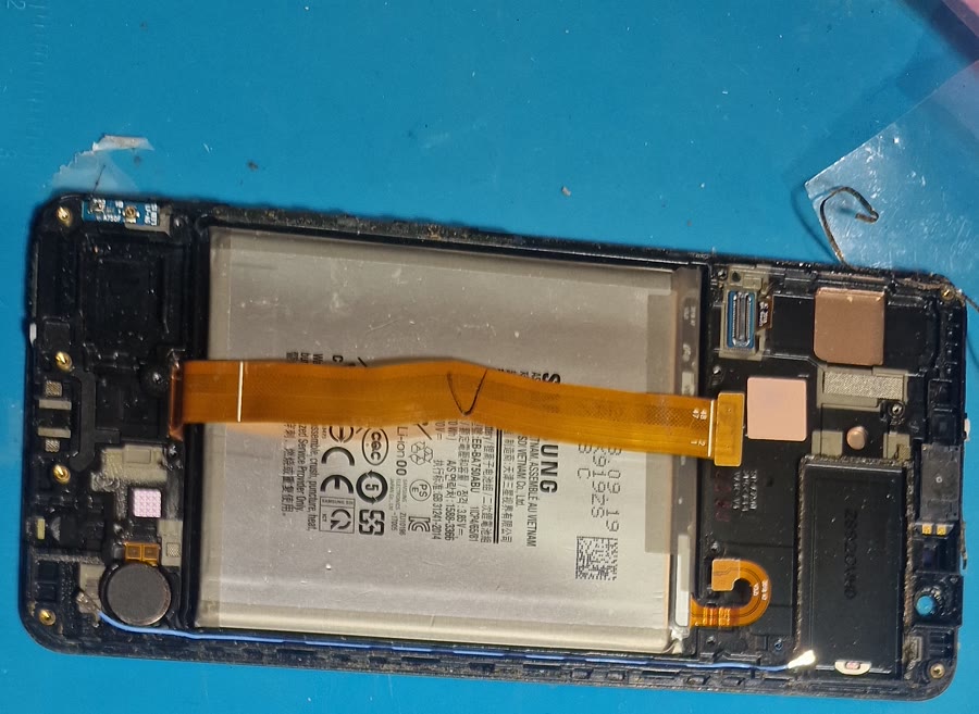 Odprt telefon z izpostavljeno baterijo in priključnim trakom na servisni podlogi