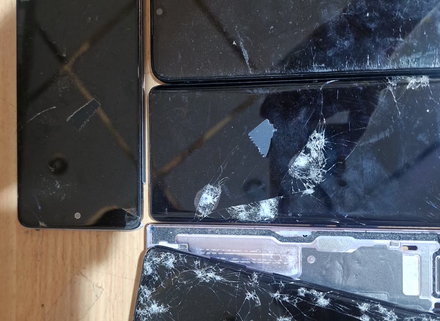 Več telefonov s počenimi in razbitimi zasloni v naši delavnici