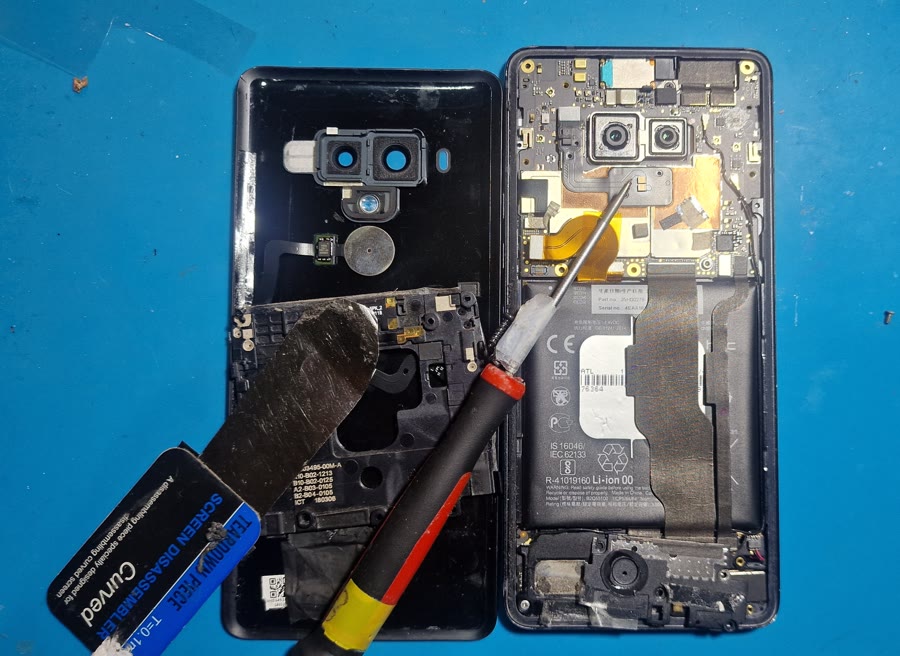 Serviser z odvijačem popravlja odprt telefon na servisni podlogi